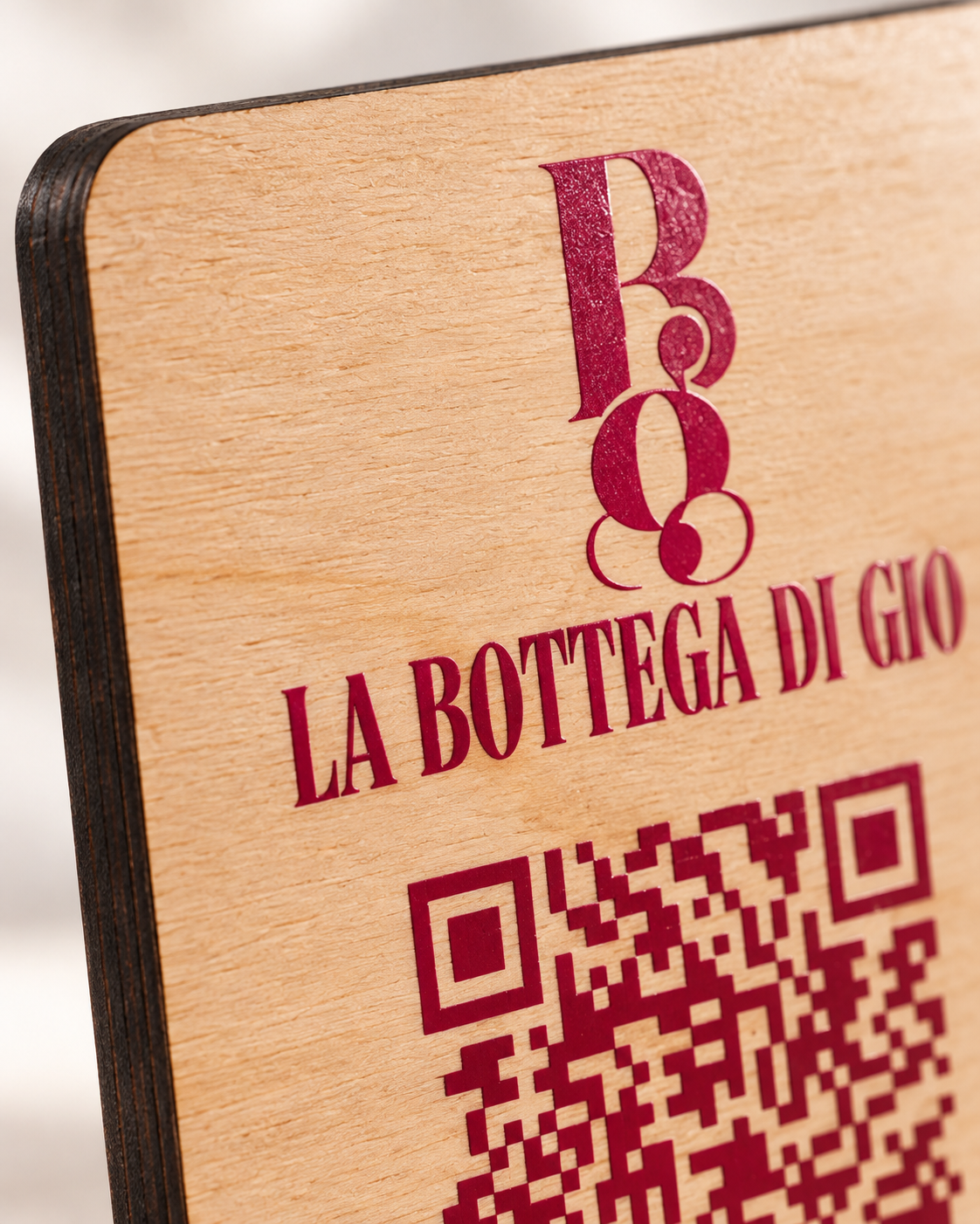 Gros plan sur un logo et un QR Code imprimés directement en UV couleur bordeaux sur une plaque en bois naturel.