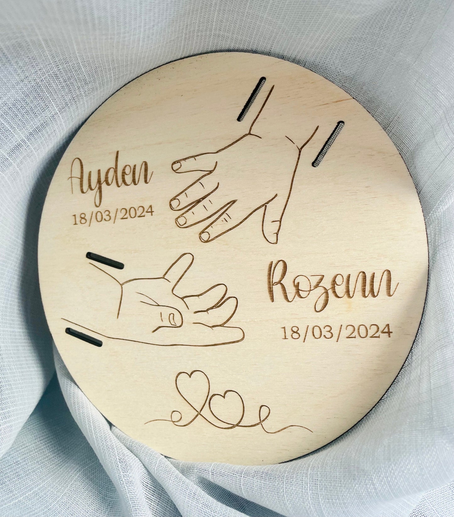 Plaque de naissance en bois gravée avec prénoms, dates et illustration des mains de la famille.